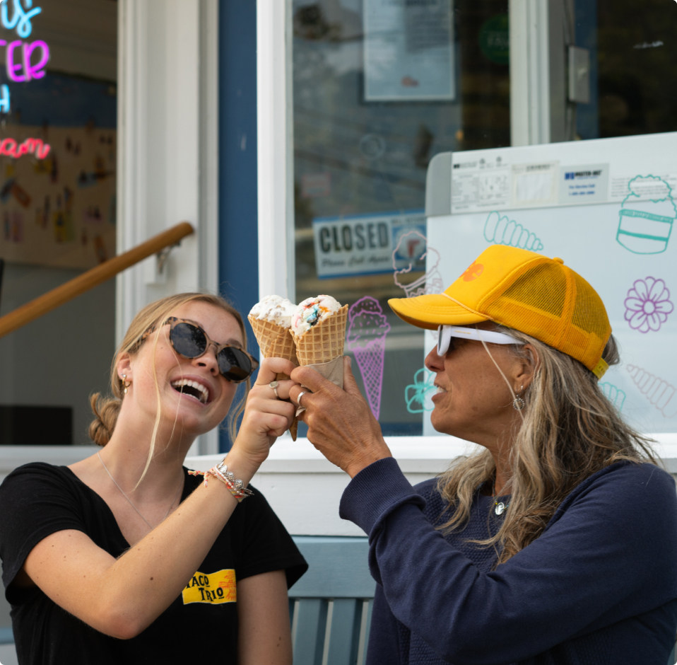 Two women laughing and toasting with ice cream cones outside a shop in Portland Maine.