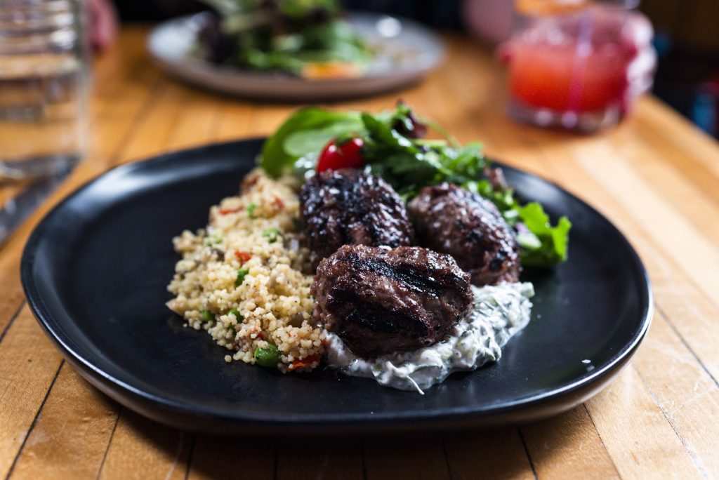 Grilled meatballs served with couscous, tzatziki sauce, and a fresh green salad in Portland Maine.