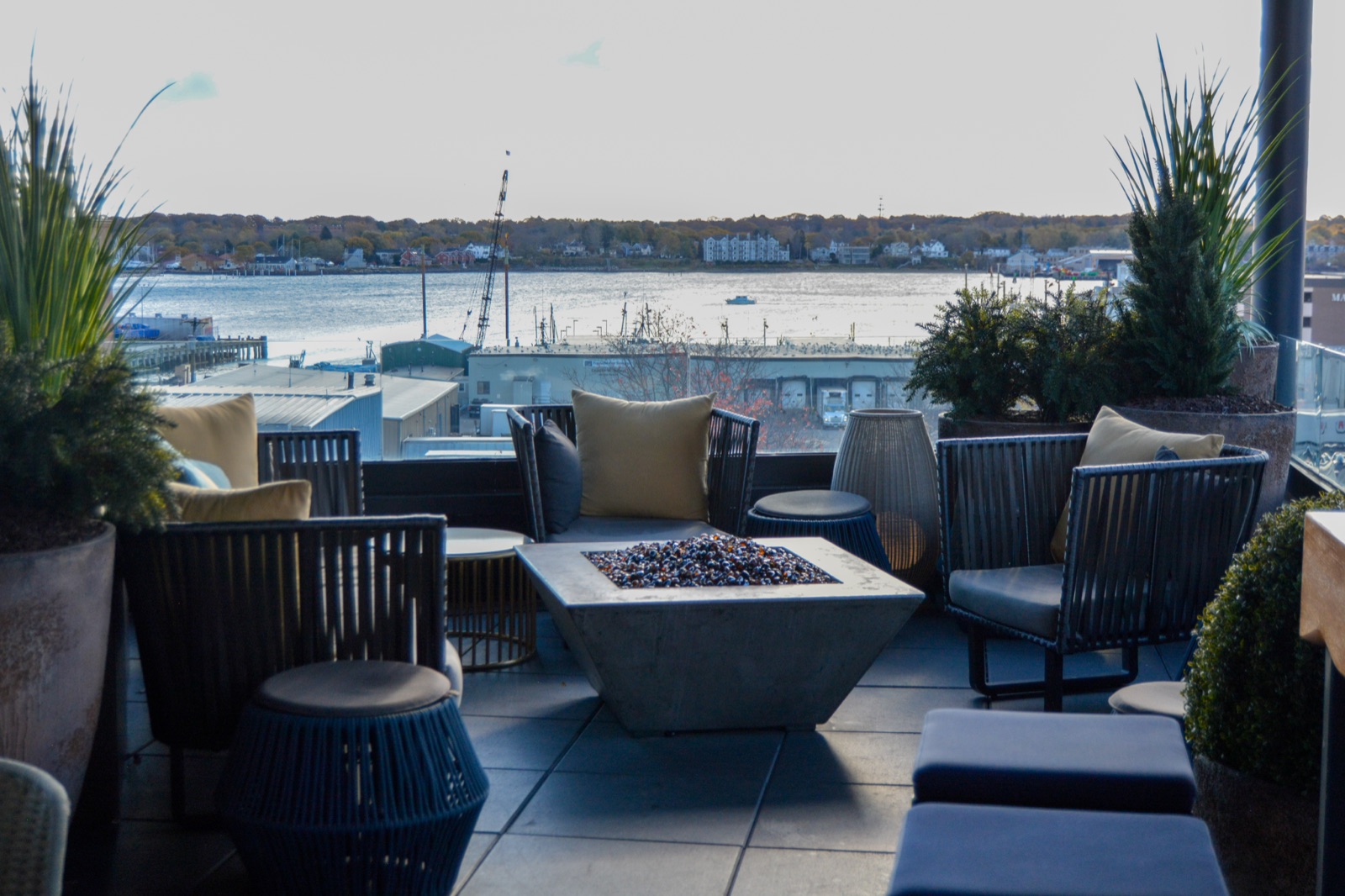 A rooftop patio with a fire pit overlooking a harbor and distant town in Portland Maine.