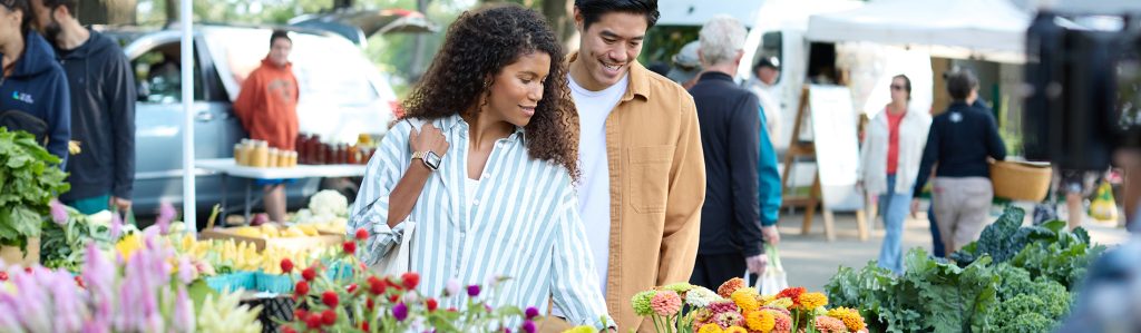 A couple shops for fresh flowers at an outdoor farmers market in Portland Maine.