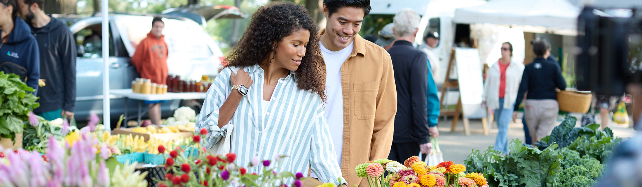 A couple shops for fresh flowers at an outdoor farmers market in Portland Maine.
