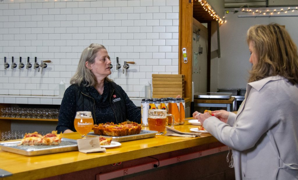 A woman behind a bar serves pizza and beer to a customer in Portland Maine.