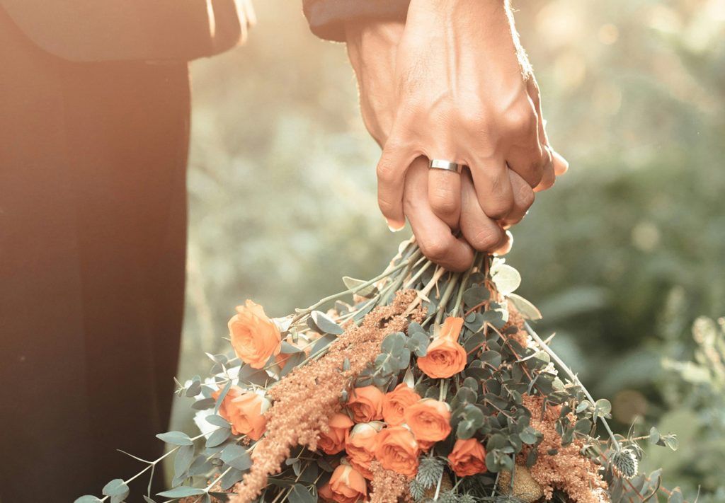 A couple holding hands while carrying a bouquet of orange roses in Portland Maine.
