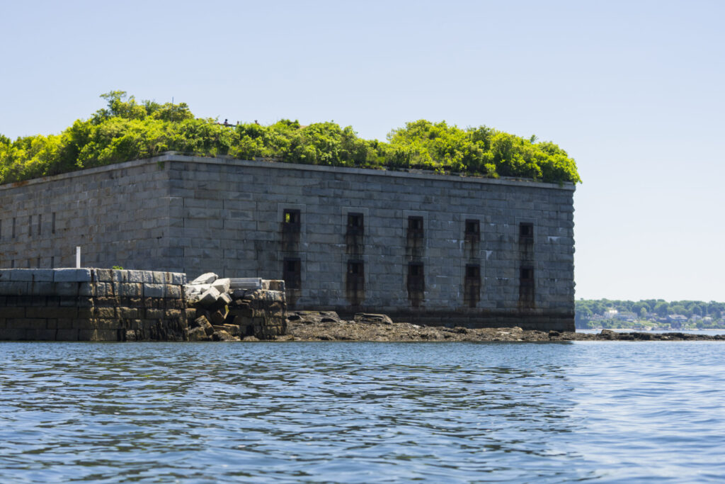 A stone fortress with a green, tree-covered roof sits by the water in Portland Maine.
