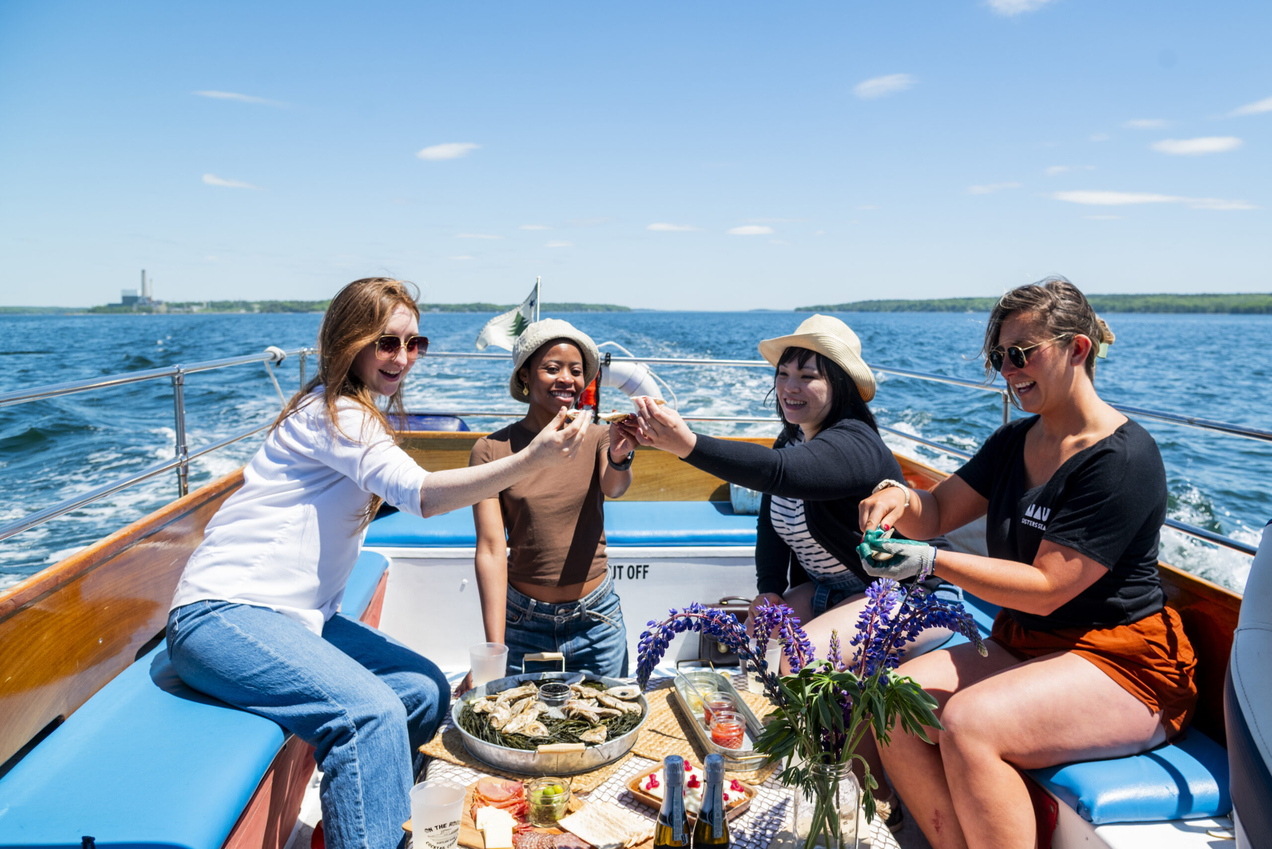 Four women enjoy a boat ride while eating oysters on a sunny day in Portland Maine.