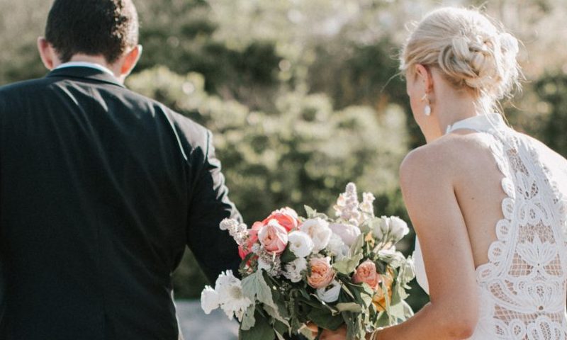 A bride and groom walking together outdoors, with the bride holding a floral bouquet in Portland Maine.