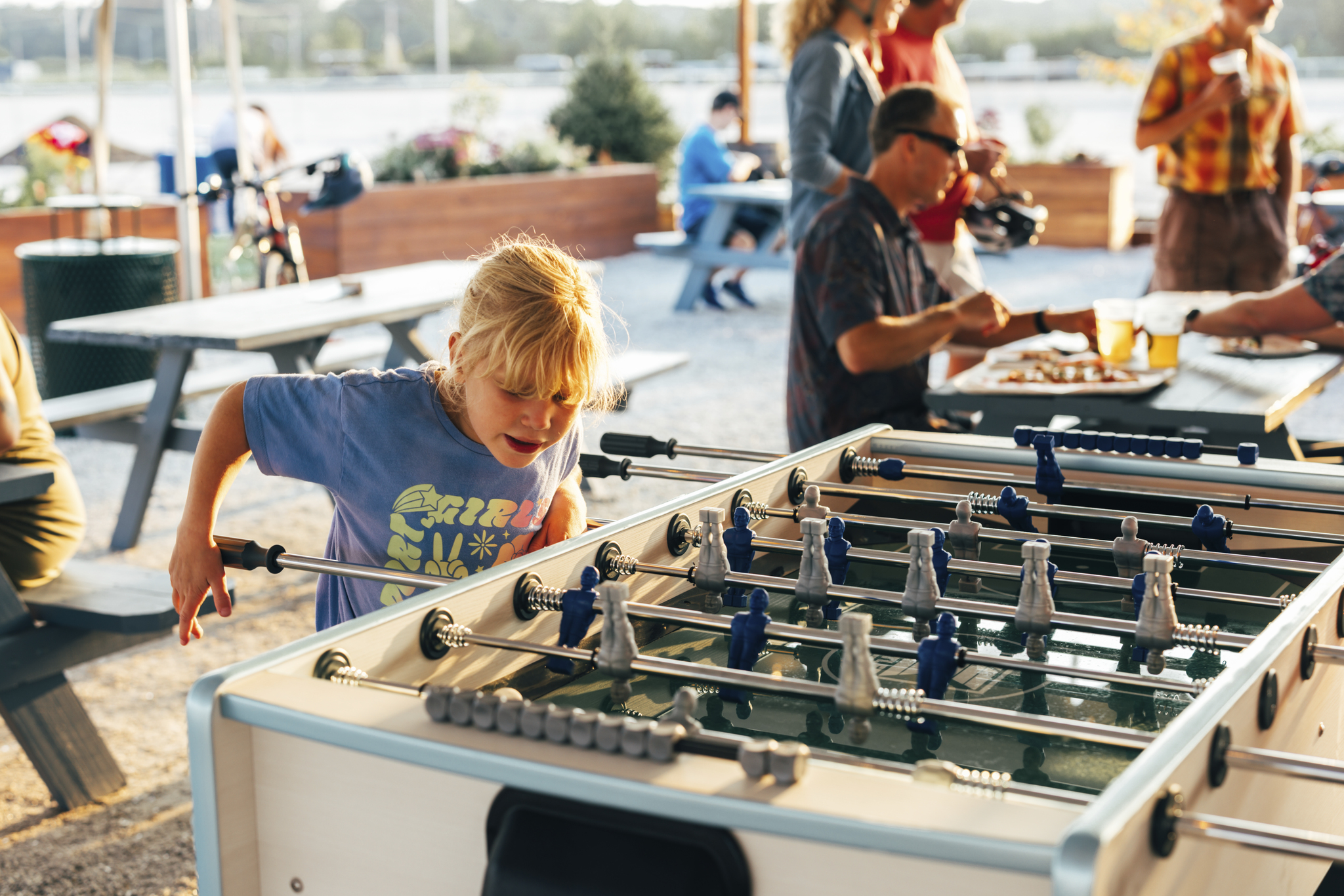 A young blonde girl focused on playing a game of foosball outdoors in Portland Maine.