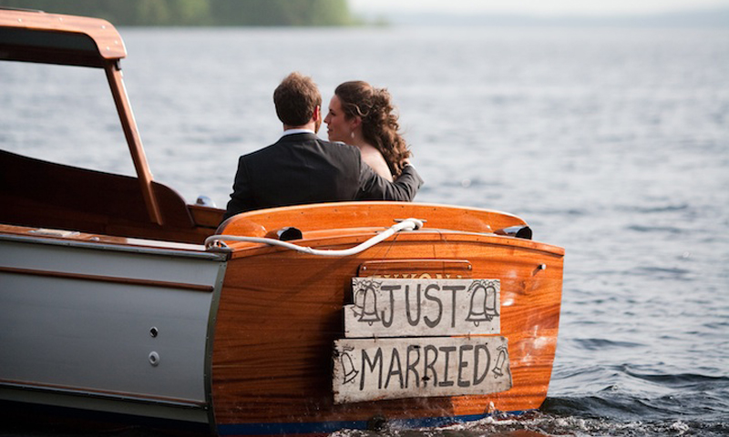A newlywed couple sits in a wooden boat with a just married sign in Portland Maine.