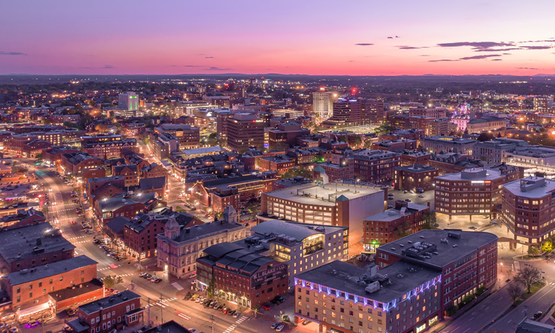 An aerial view of a city skyline at sunset with illuminated buildings and streets in Portland Maine.