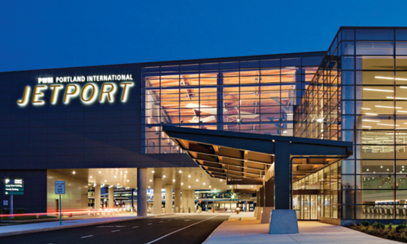 The exterior of Portland International Jetport at dusk with illuminated signage in Portland Maine.