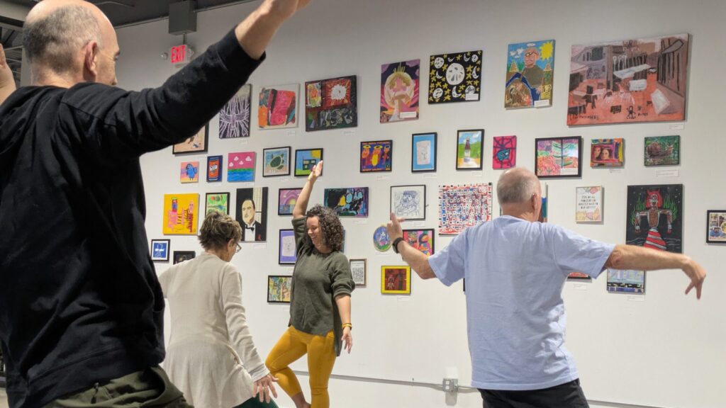 Three people practicing yoga poses in front of a wall covered with framed artwork in Portland Maine.