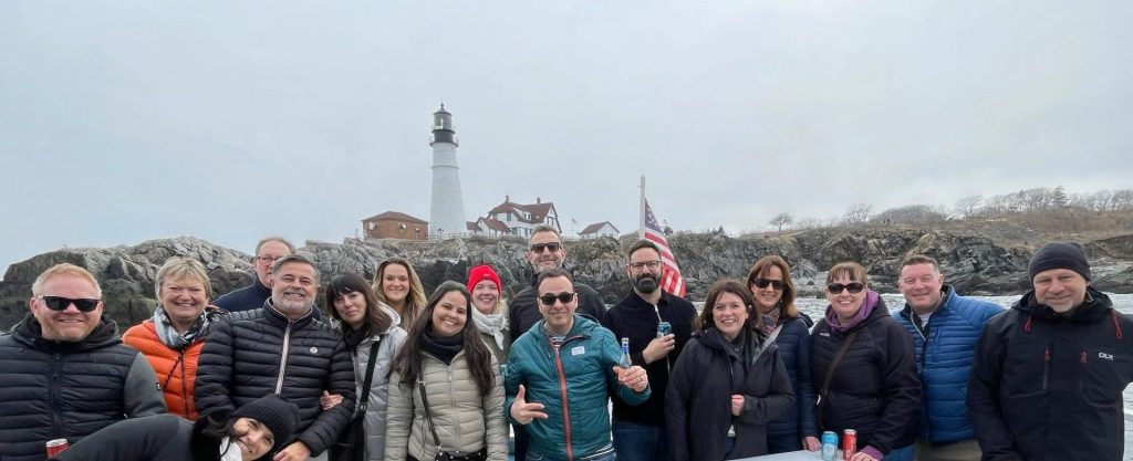 A group of people posing for a photo in front of a coastal lighthouse in Portland Maine.