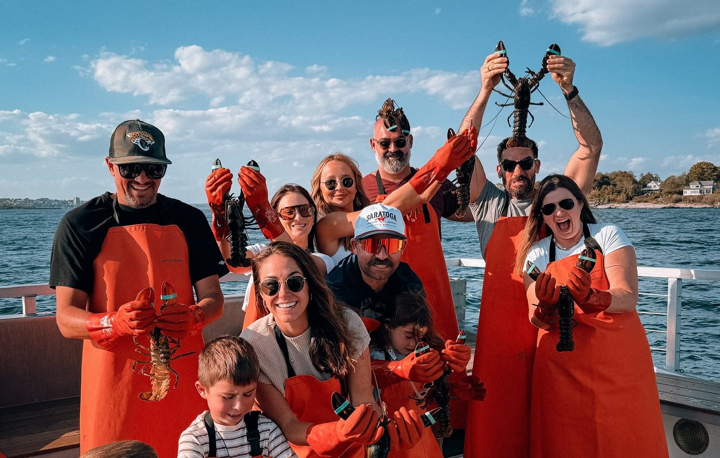 A group of people wearing orange aprons and gloves holding lobsters on a boat in Portland Maine.