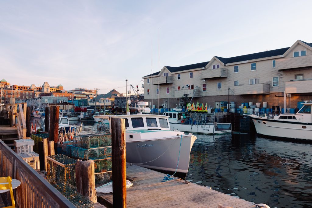 Fishing boats docked at a harbor with lobster traps on the wooden pier in Portland Maine.