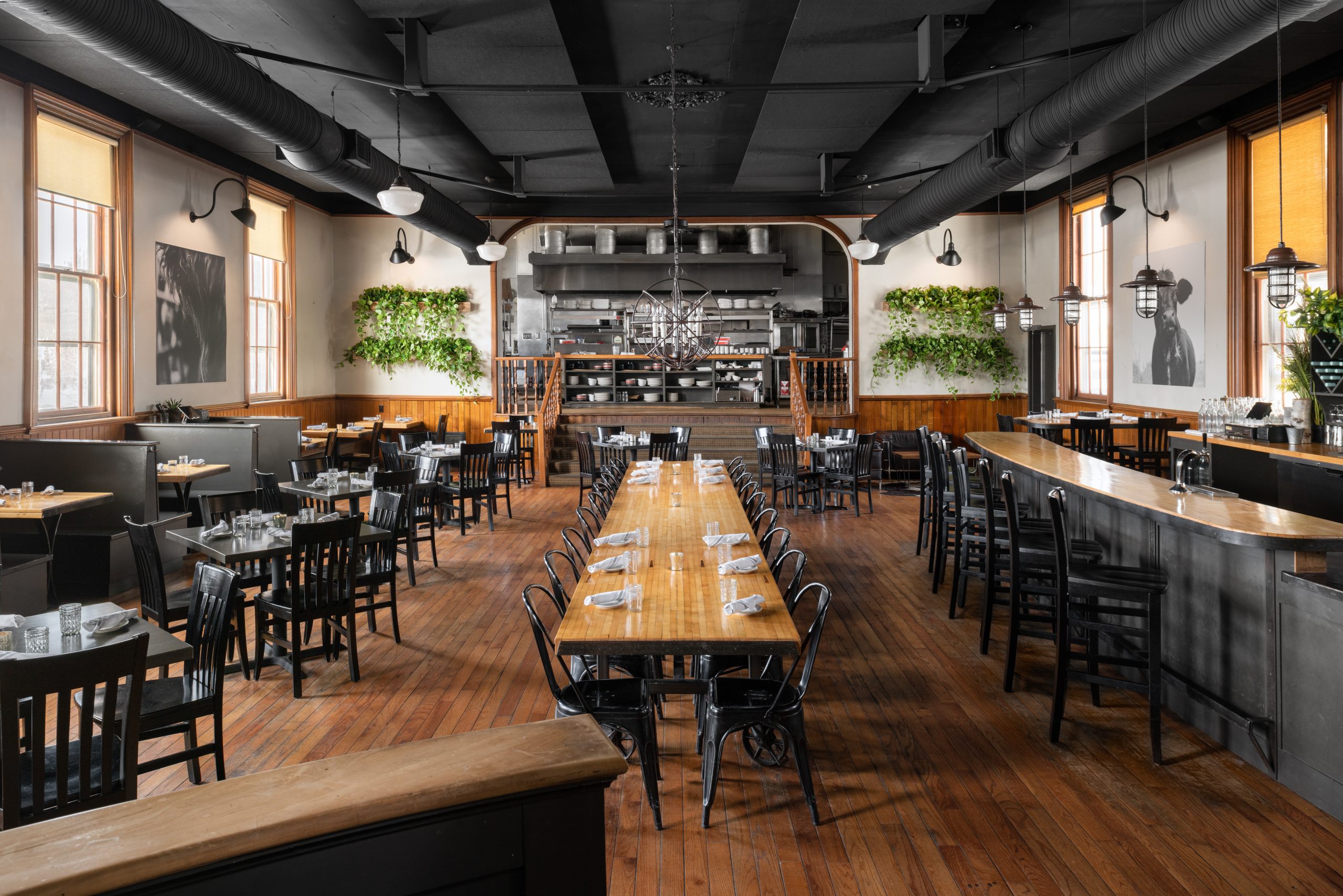 A spacious restaurant interior with wooden tables, black chairs, and an open kitchen in Portland Maine.