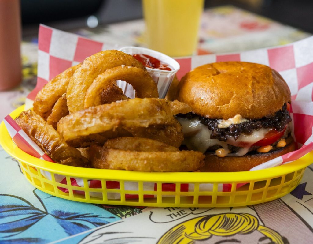 A cheeseburger and onion rings served in a yellow plastic basket with ketchup in Portland Maine.