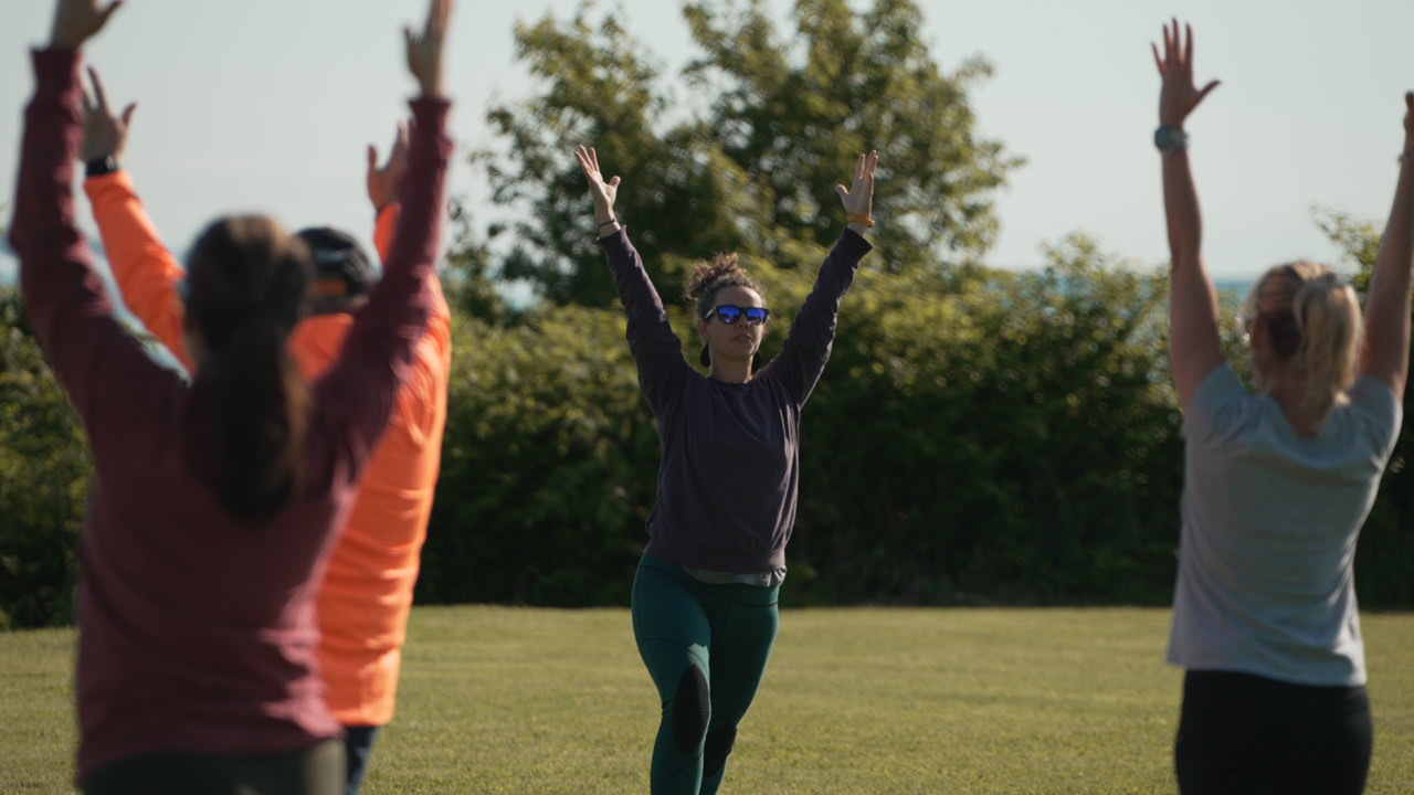 A group of people practicing yoga outdoors with arms raised in a grassy field in Portland Maine.