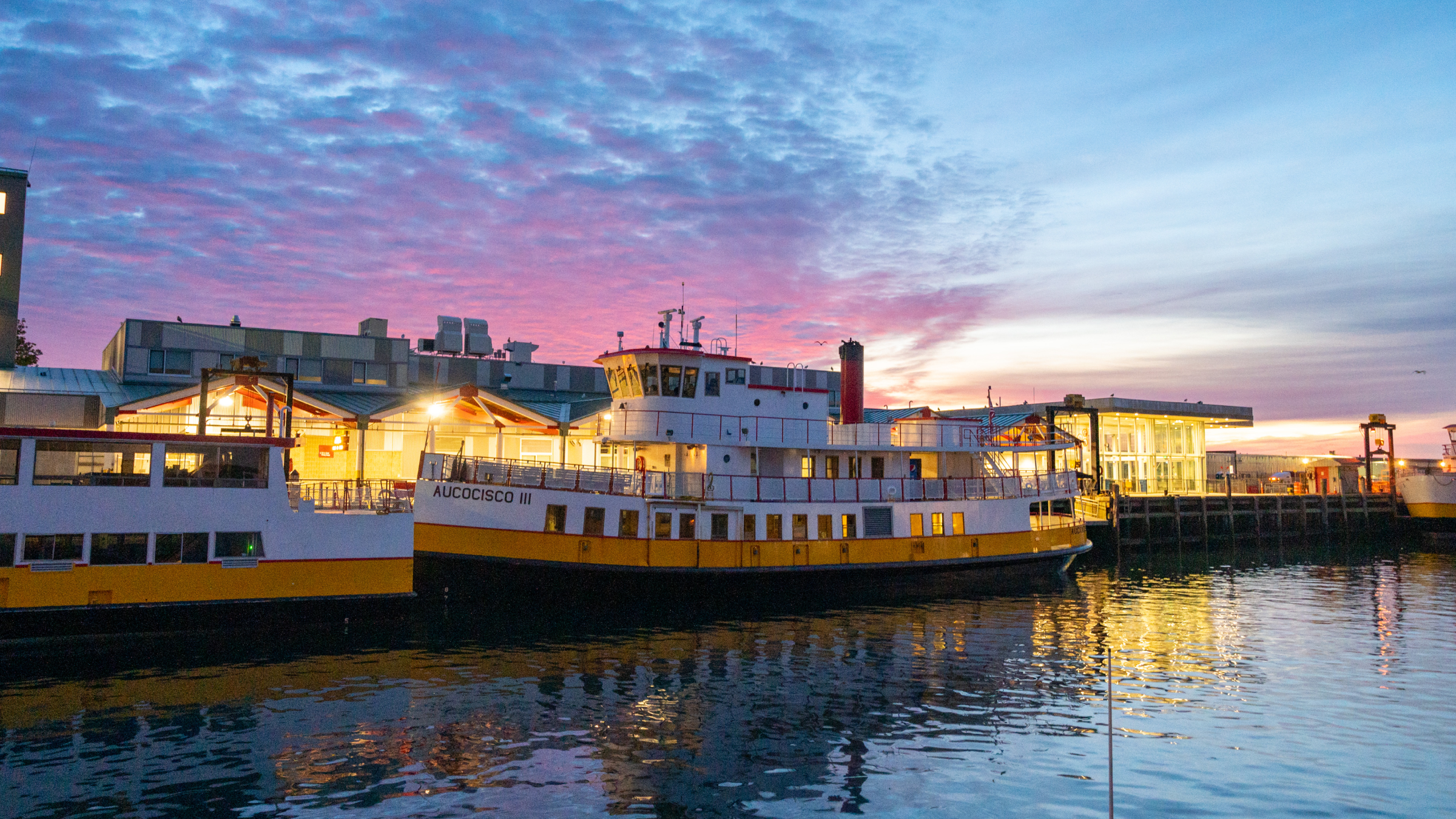 The Aucocisco III ferry docked at a pier during a vibrant sunset in Portland Maine.