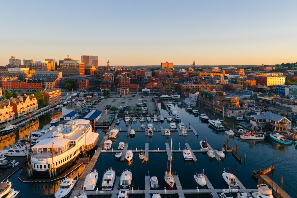 An aerial view of a marina filled with boats at sunset near a city in Portland Maine.