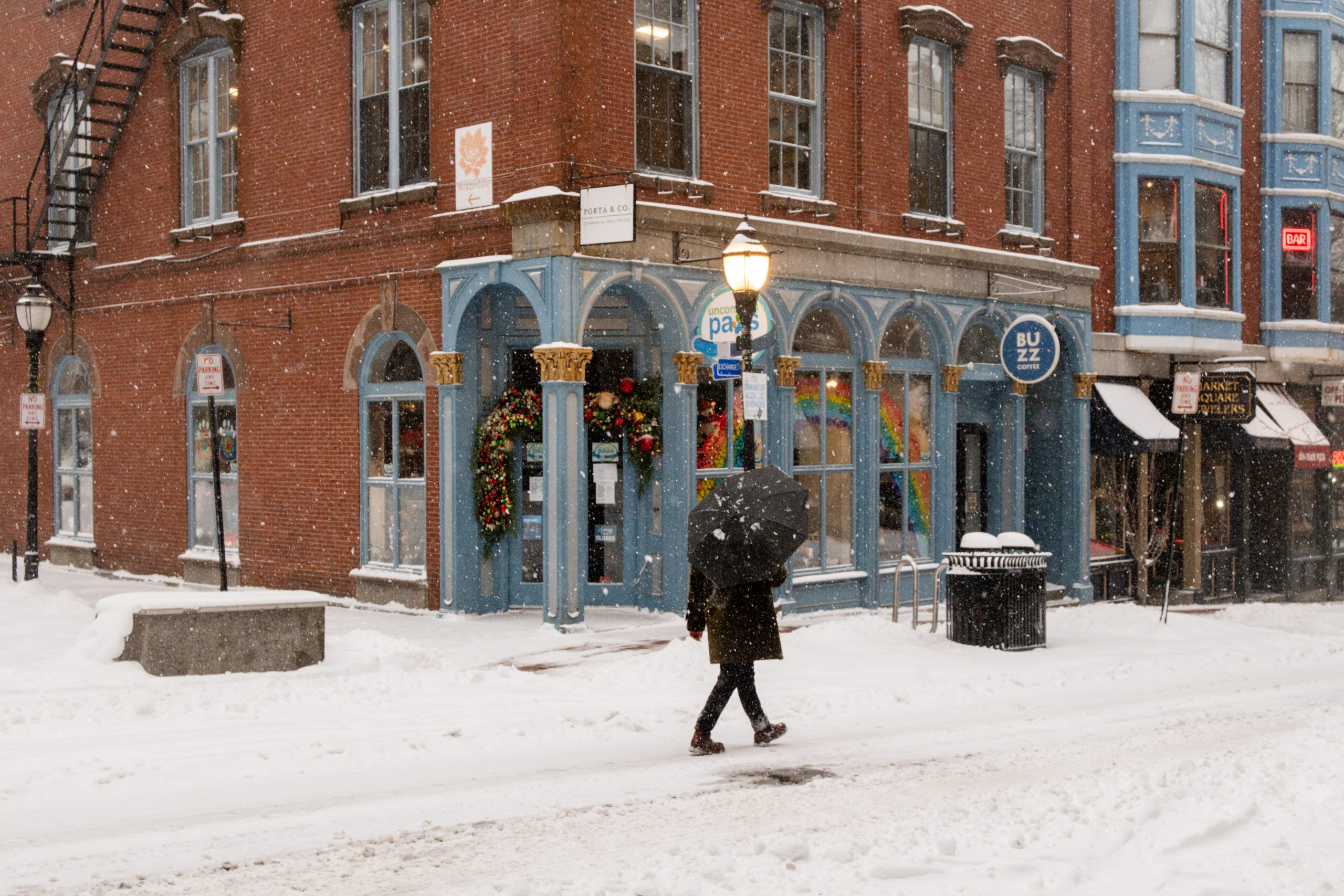 A person with an umbrella walks past a snow-covered brick building during a storm in Portland Maine.