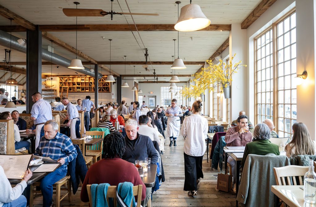 A busy, well-lit restaurant interior with patrons dining and staff serving in Portland Maine.