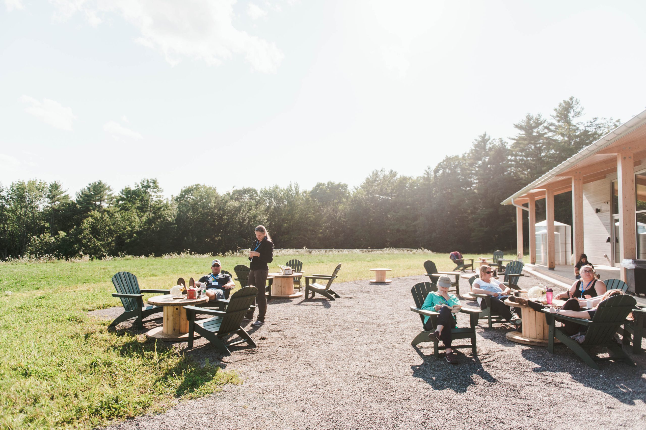 People sitting in Adirondack chairs on a gravel patio outside a building in Portland Maine.