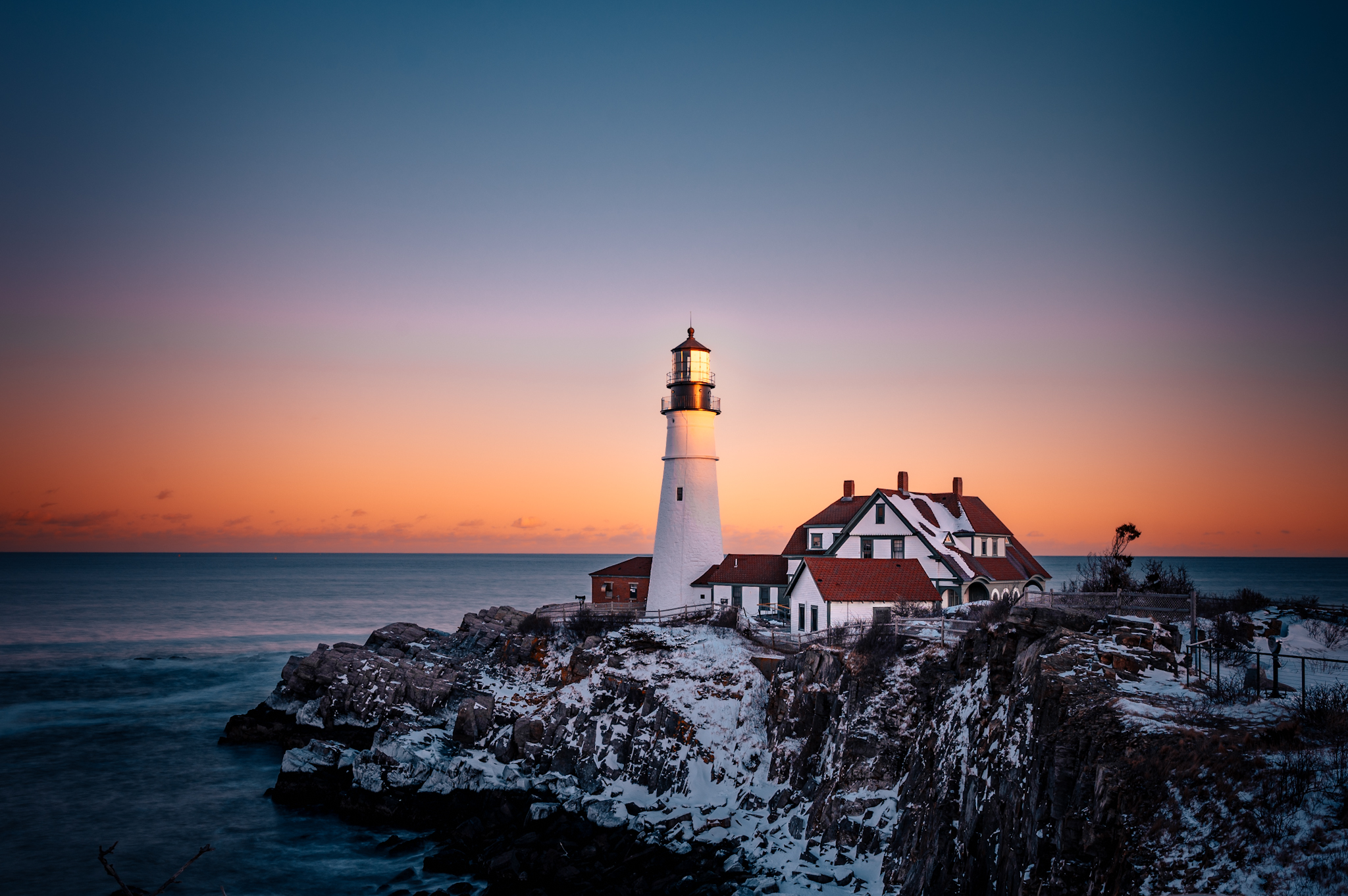 A lighthouse and buildings on a snowy cliff at sunset in Portland Maine.