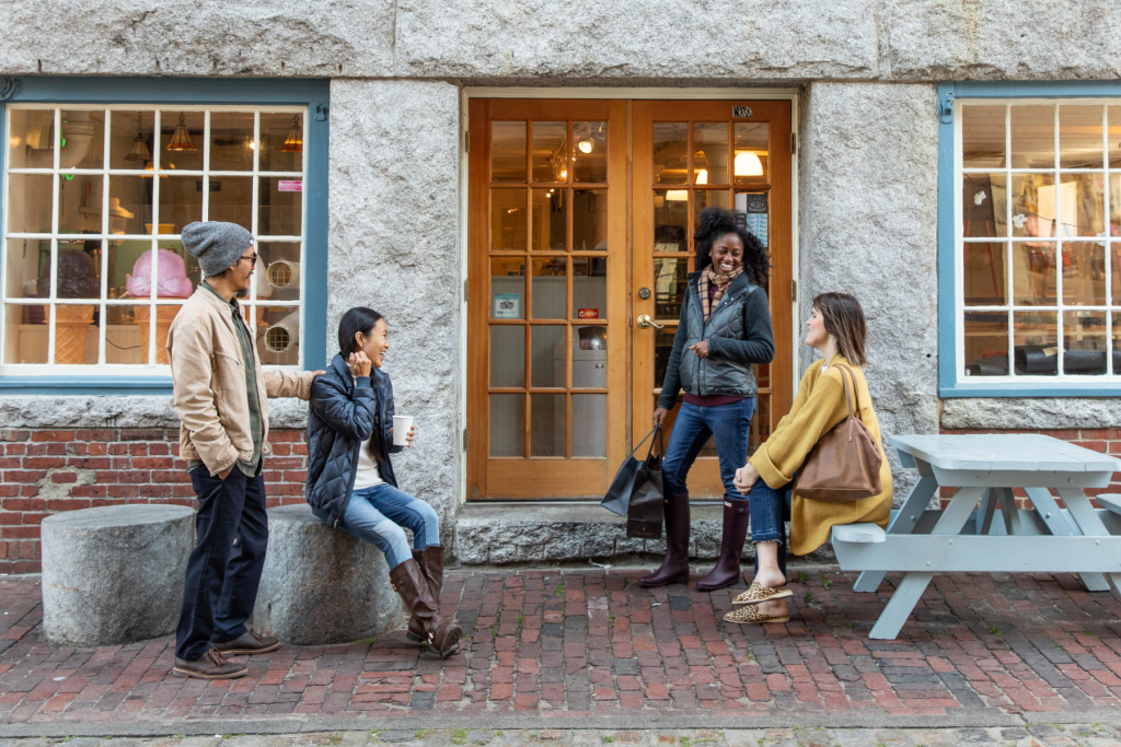 Four friends chatting outside a storefront with stone walls and a wooden door in Portland Maine.