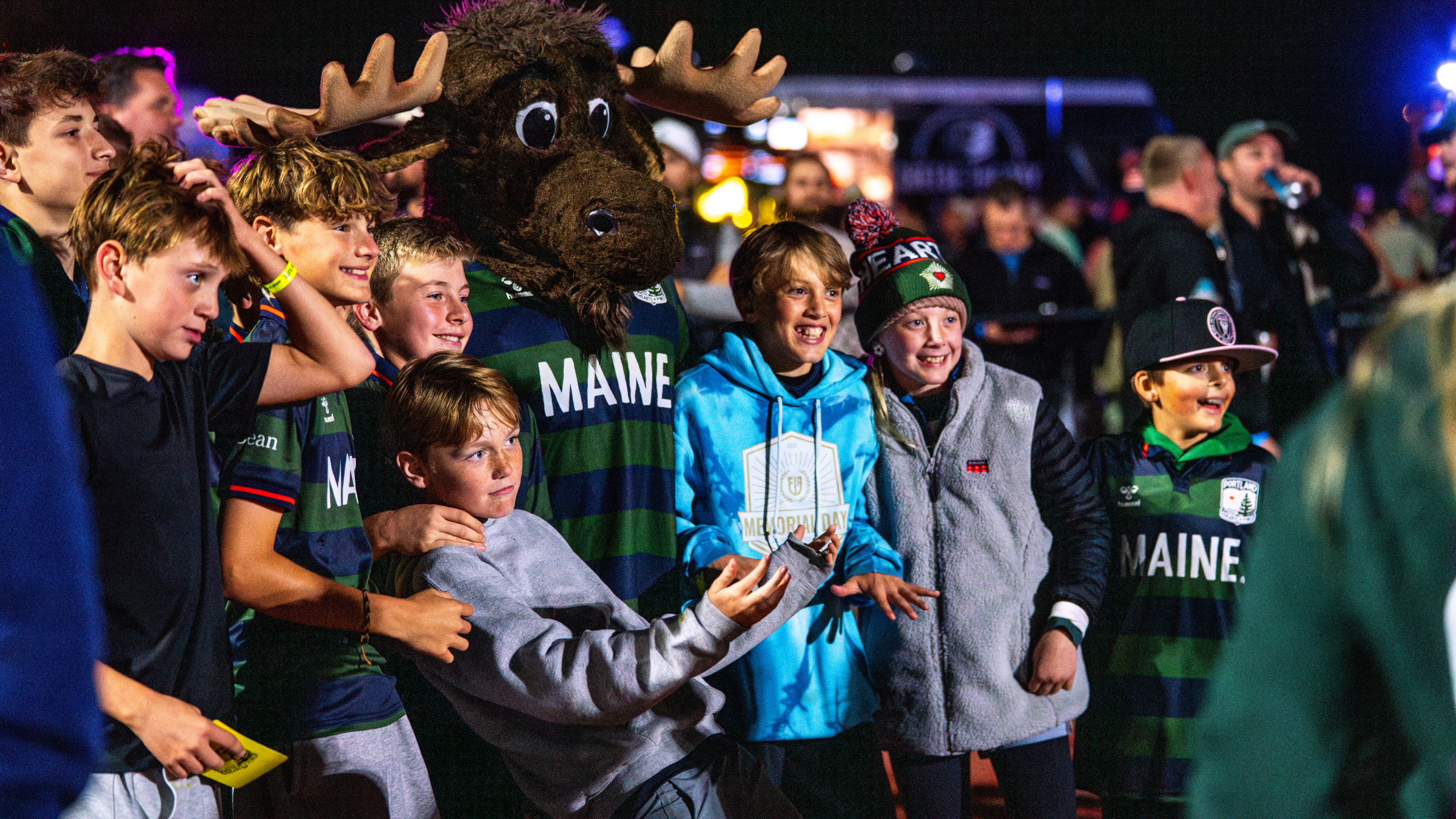 A group of children posing for a photo with a Maine mascot at night in Portland Maine.