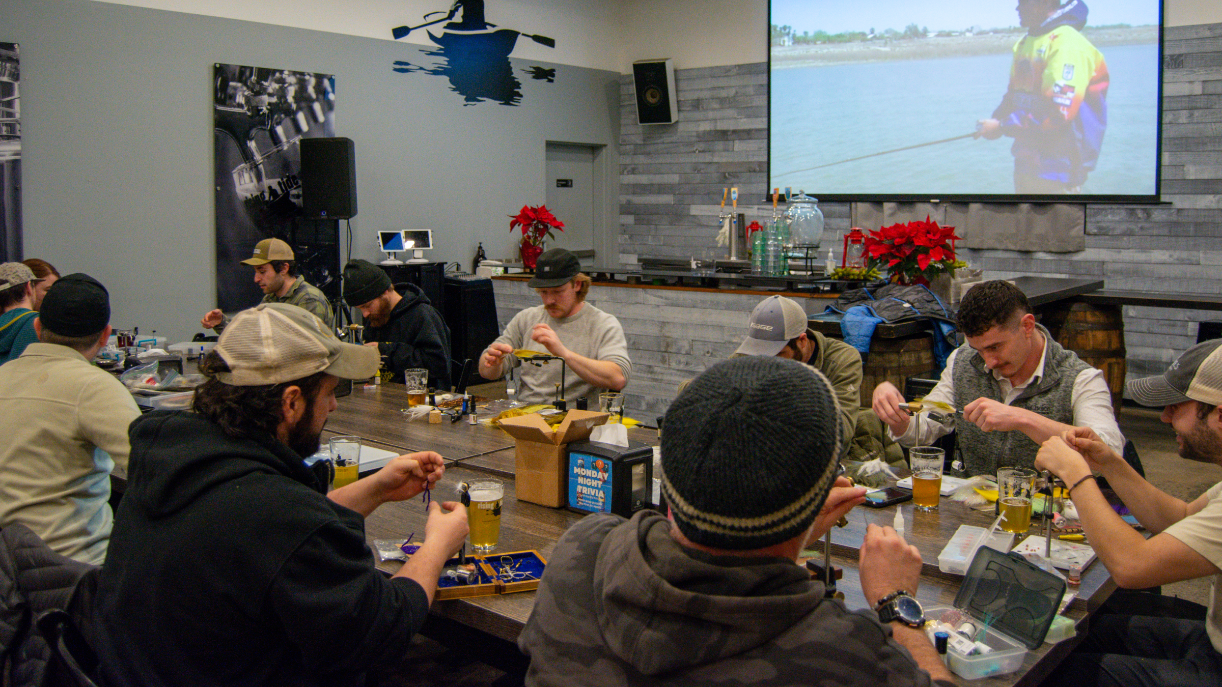 A group of people sitting at a long table learning to tie fishing flies in Portland Maine.