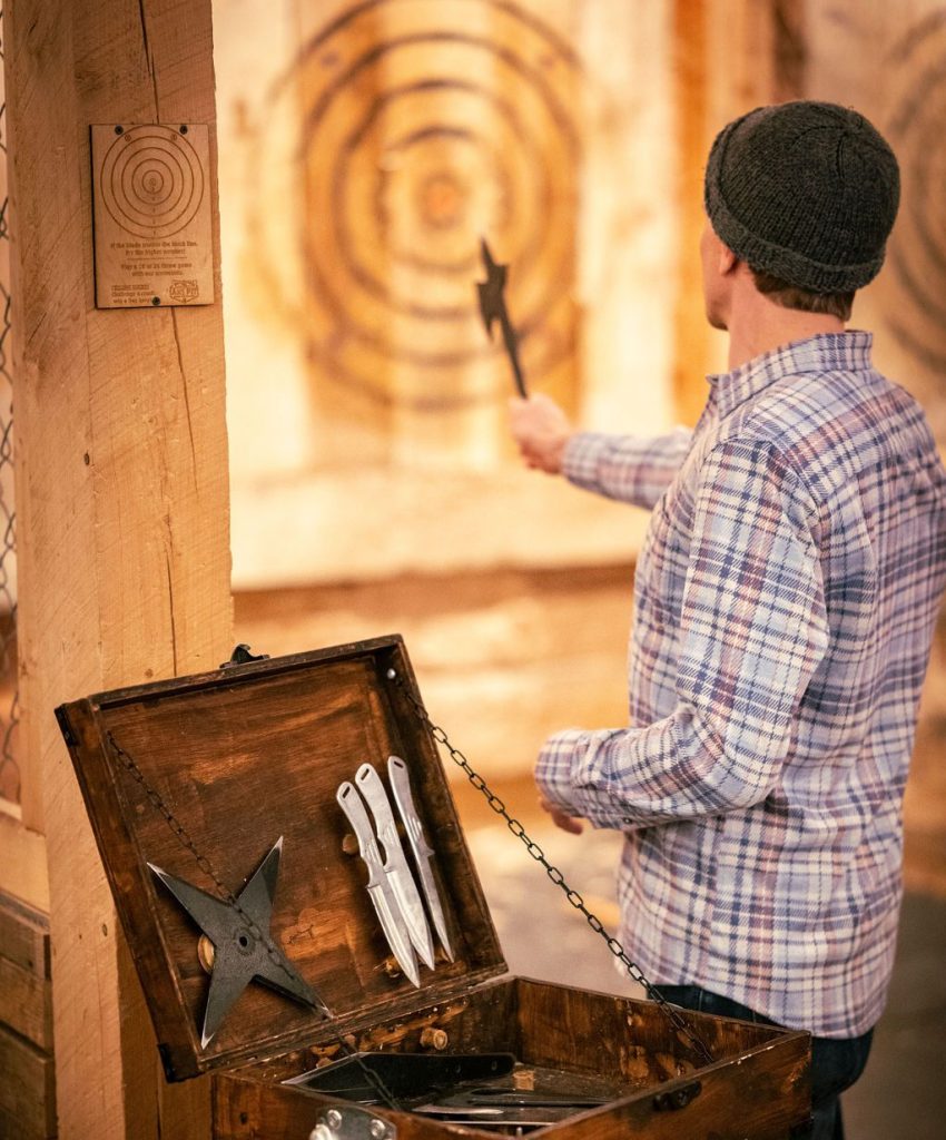 A man in a plaid shirt throws an axe at a wooden target at The Axe Pit in Portland Maine.