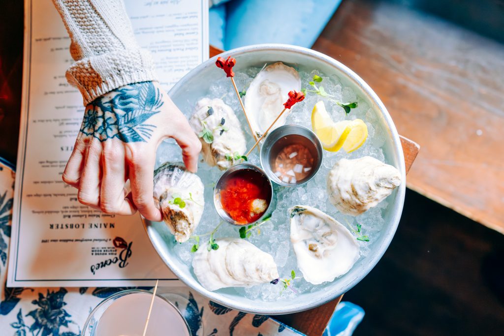 A tattooed hand reaches for a fresh oyster from a bowl of ice in Portland Maine.