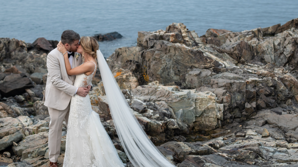 A bride and groom kissing on a rocky coastline by the ocean in Portland Maine.