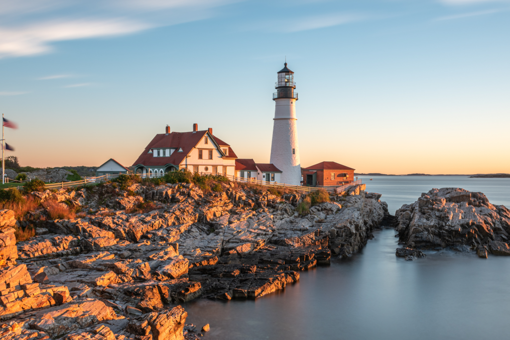 A white lighthouse stands on a rocky coastline during a golden sunset in Portland Maine.