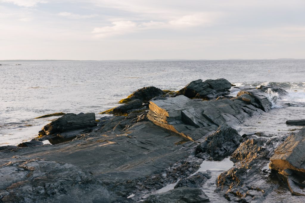 Jagged dark rocks along a calm ocean coastline at sunset in Portland Maine.