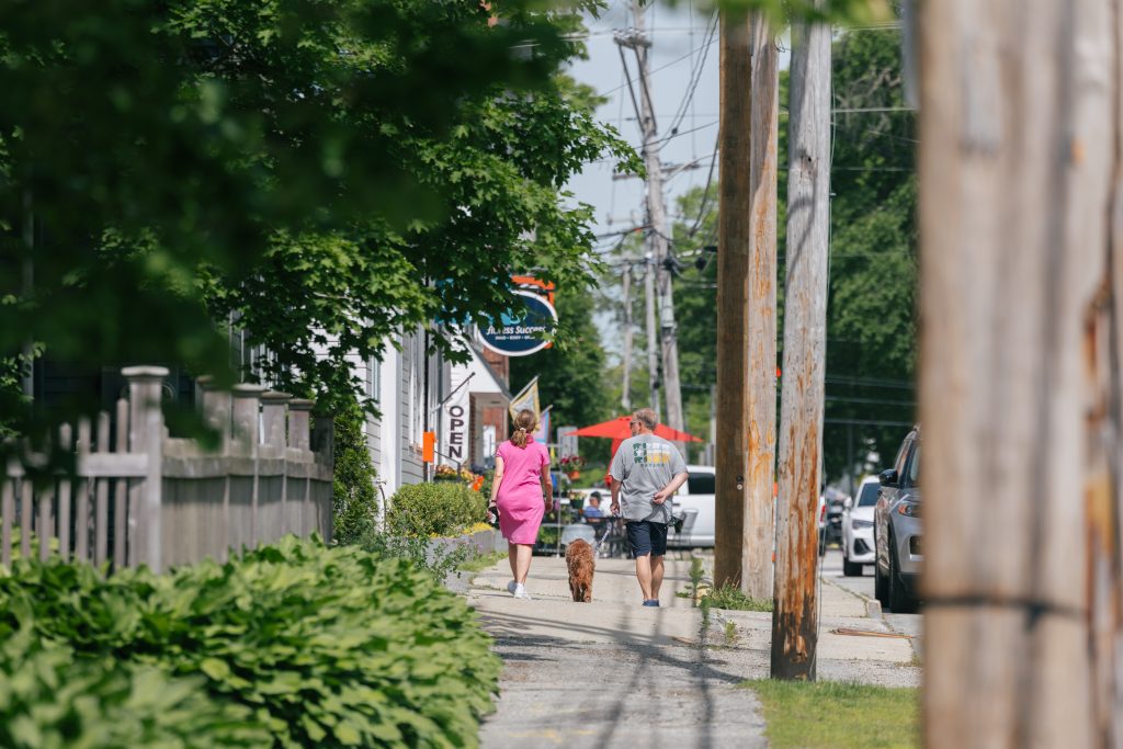 A couple walks their dog along a sunny sidewalk on Yarmouth's Main Street.