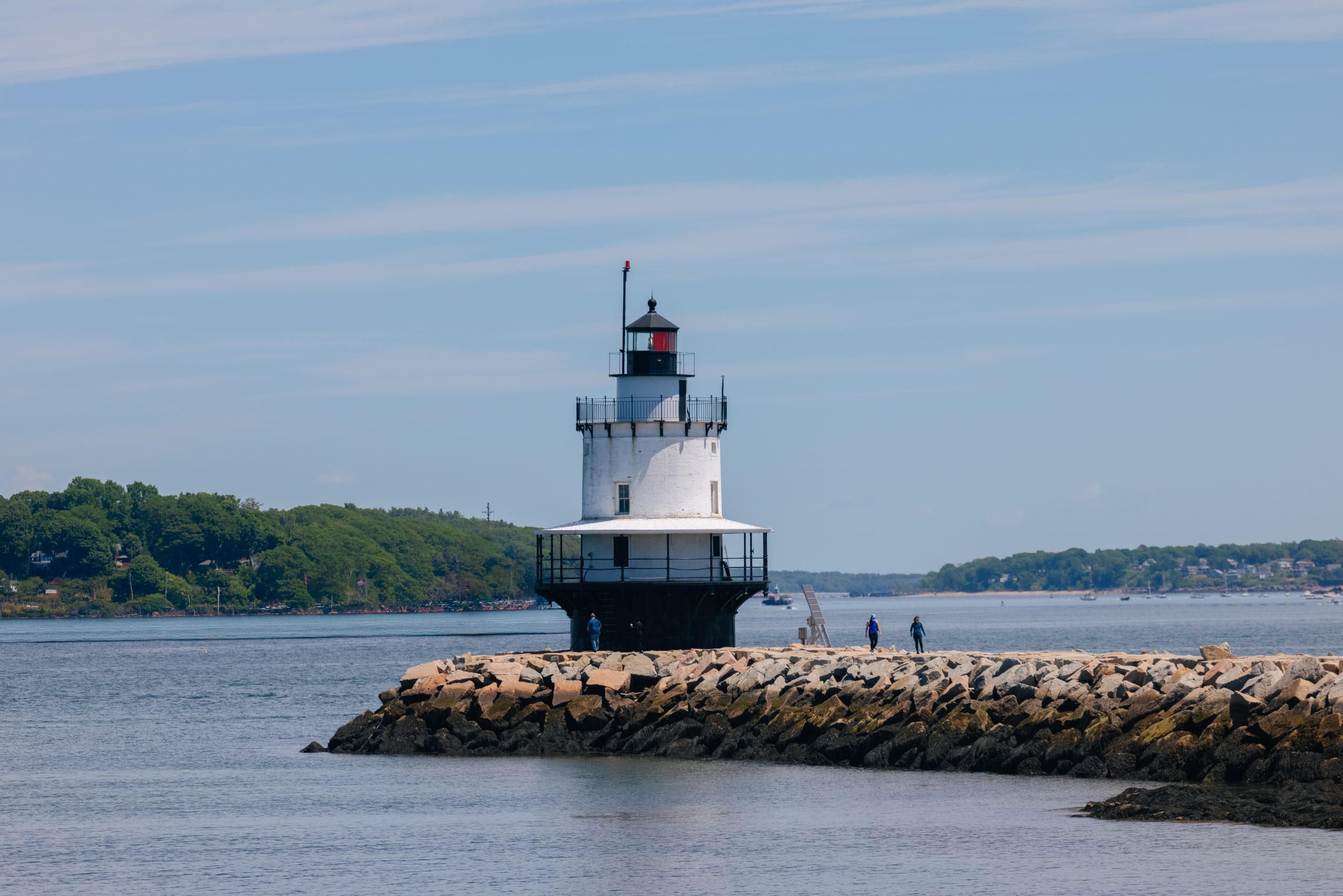 A white lighthouse stands on a rocky breakwater surrounded by water in Portland Maine.
